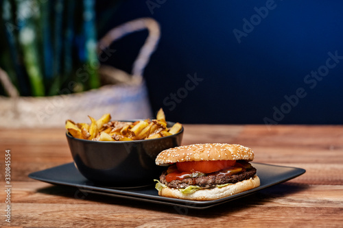 Homemade burger with fries on a dark plate and wooden table background.