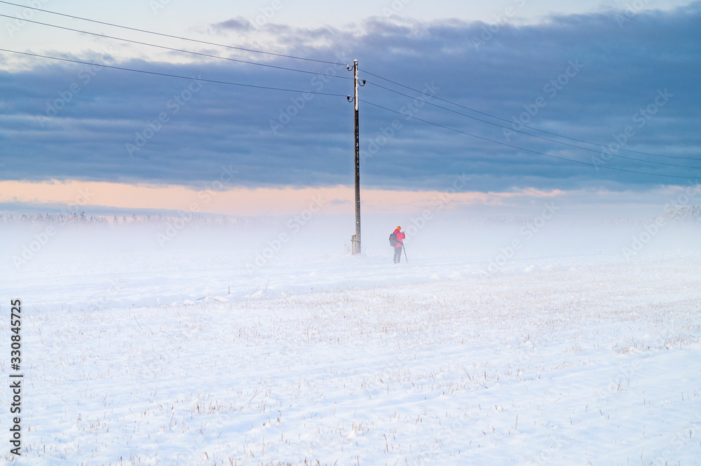 Winter sunrise over snow covered field with a layer of fog and a person in distance.. Winter sunrise over snow covered field with a layer of fog and a person in distance..