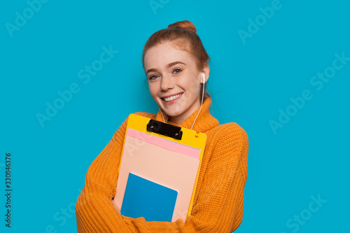 Canvas Print Cheerful red haired caucasian student with freckles is holding some books and po