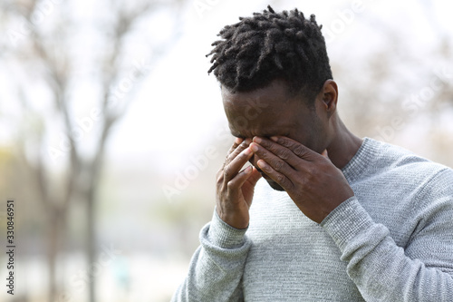 Black allergic man scratching itchy eyes in a park
