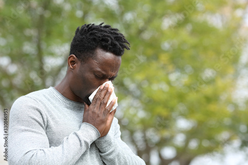 Allergic black man blowing on wipe in a park on spring season photo
