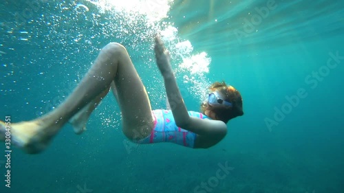Beautiful girl swimming under the ocean's surface with air bubbles and sunlight, active healthy fitness lifestyle. 