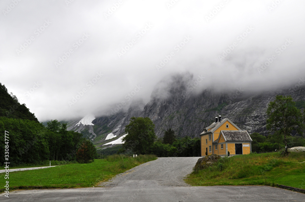 Old wooden house with road standing in mountains under thick clouds - Troll road, Norway