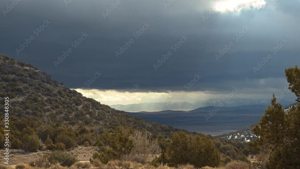 View of sun rays shining through dark clouds moving over the landscape on windy day in the desert. View of sun rays shining through dark clouds moving over the landscape on windy day in the desert.