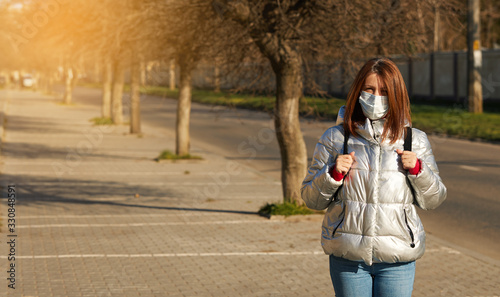 A young woman in a protective mask respirator stands in the middle of the street on a sunny day. Left empty space for text. Covid-19 Coronavirus Pandemic