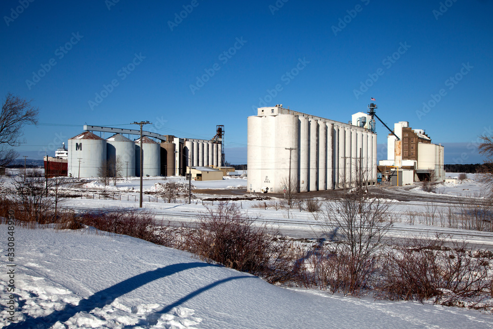 Obraz premium Winter scenic of grain storage tanks and elevators in the snow near the shoreline of Lake Superior. Superior Wisconsin WI USA