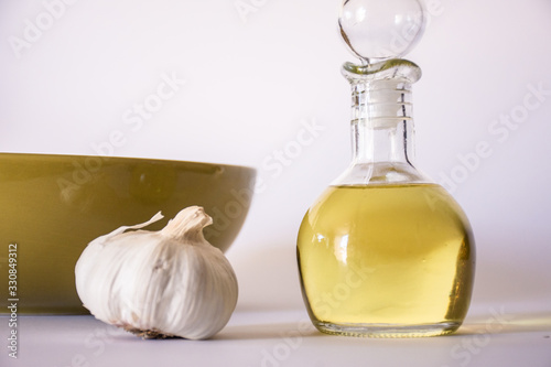Closeup of olive oil jar and garlic on white background