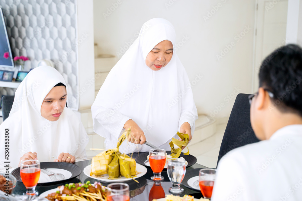 Elderly Asian woman cutting ketupat for her family Elderly Asian woman cutting ketupat for her family