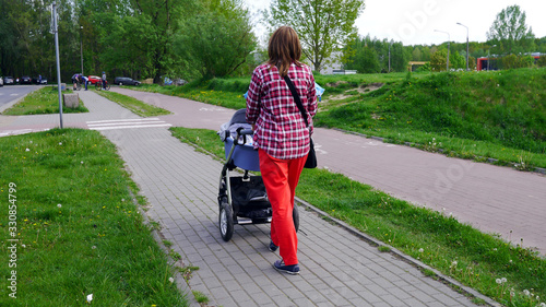 Mama z nowo narodzonym dzieckiem w wózku. Kobieta spaceruje w parku blisko lasu. Dziecko na świeżym powietrzu, dbanie o zdrowie dziecka. Noworodek śpi na spacerze. Urlop macierzyński. Słoneczny dzień.