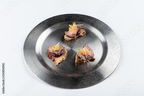 Beef canapes with beetroot sauce on black plate isolated on white background for a menu