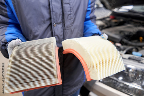 New and old dirty automotive engine air filter in the hands of an auto mechanic. Auto repair concept.