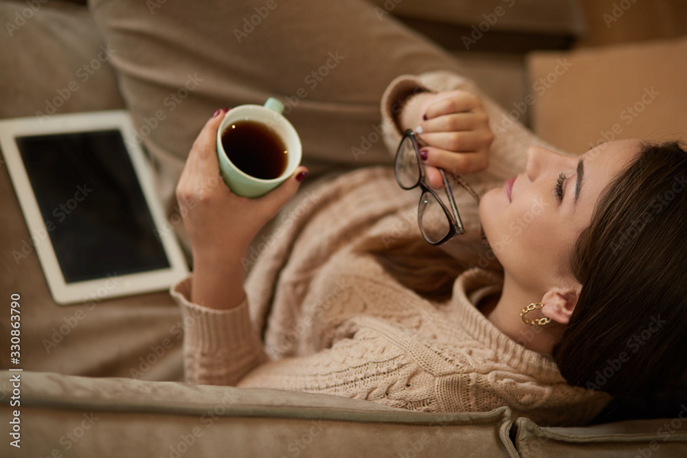 Happy young woman sitting on sofa holding a mug at home in the living room
