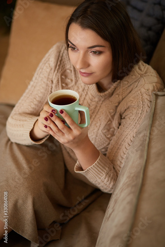 Happy young woman sitting on sofa holding a mug at home in the living room