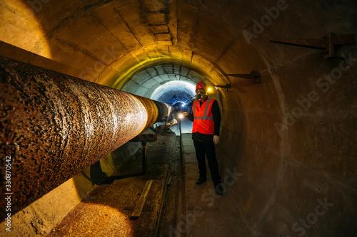 Tunnel worker examines pipeline in underground tunnel photo