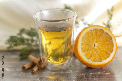 Vitamin lemon yellow tangerine peel drink in a transparent glass. Cinnamon and sliced orange on a wooden table. Juniper sprig