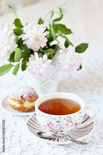 A tea party  in the style of Shabby Chic. tea in the beautiful tea steam with a pattern  rose . Delicate pink roses in a vase  white kettle in retro style. On a white lace tablecloth. Soft focus.