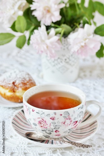 A tea party in the style of Shabby Chic. tea in the beautiful tea steam with a pattern "rose". Delicate pink roses in a vase, white kettle in retro style. On a white lace tablecloth. Soft focus.
