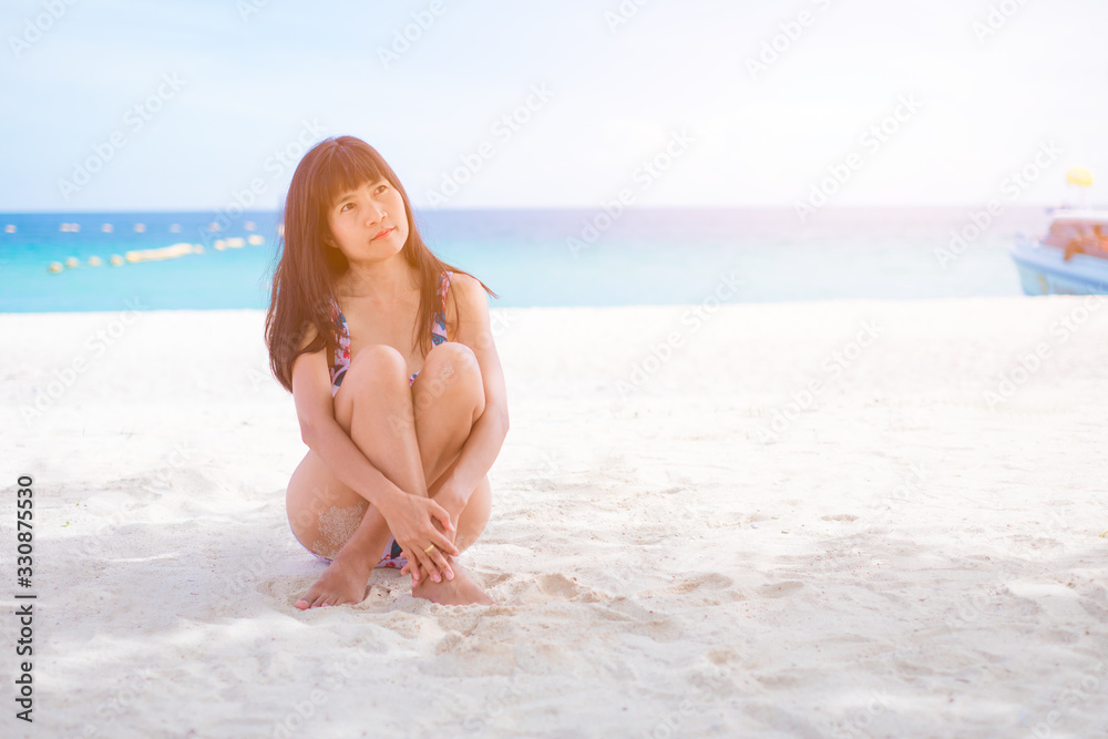 Asian women siting on sea beach with swimming suit she happy of outdoor summer on sand beach with blue sky and sea, well editing text present for your project with tourism and travel on summer season