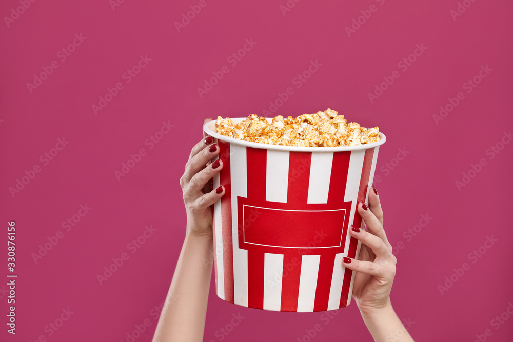 Crop of female holding bucket with popcorn on pink background.