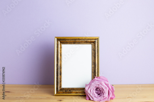Photo frame with purple rose on wooden table with pastel purple background. Anniversary concept, floral arrangement, copy space
