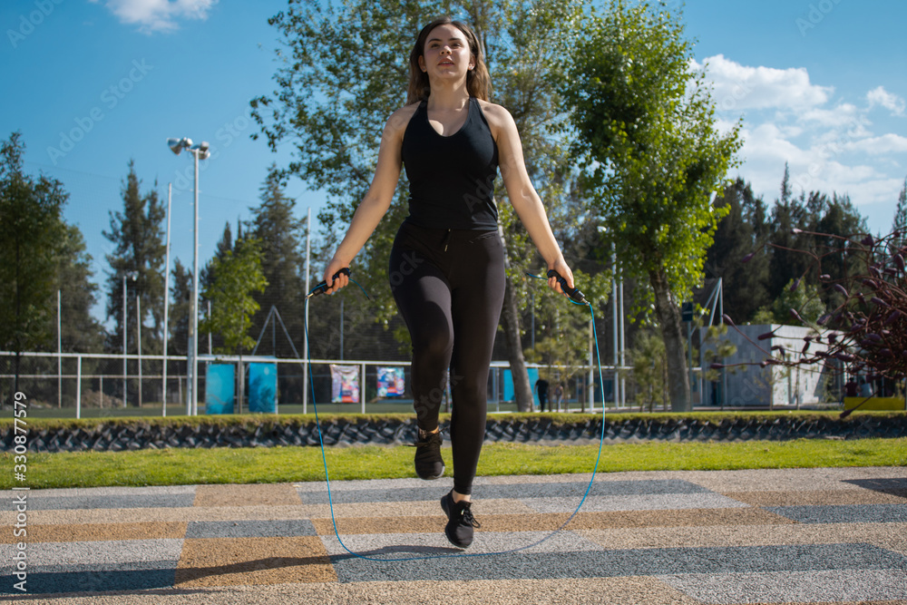 Mujer fitness con vestimenta oscura brinca la cuerda durante un día soleado Mujer fitness con vestimenta oscura brinca la cuerda durante un día soleado