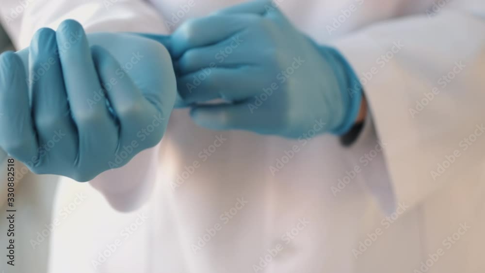 Doctor in a robe is putting medical blue gloves on. Doctor in a robe is putting medical blue gloves on.