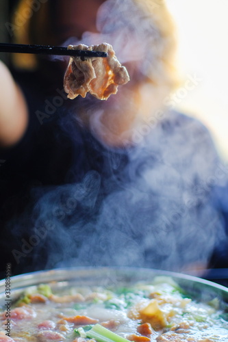 Woman holding sliced beef meat by chopsticks shabu shabu is Korean or Japanese style beef in hot pot dish of thinly sliced meat and vegetables boiled in water. delicious food most popular in thailand. photo