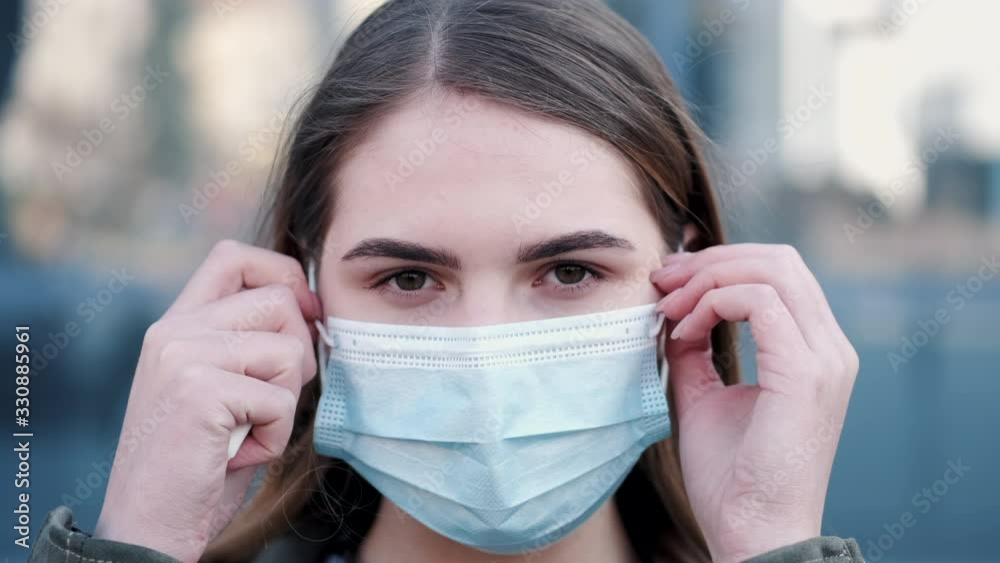 Young woman standing outside is sneezing and wearing a disposable mask. Young woman standing outside is sneezing and wearing a disposable mask.