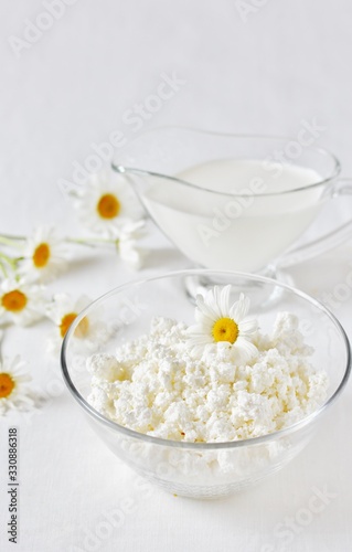 Homemade cottage cheese and cream in glassware. on a white background. Soft focus. Chamomile flowers as a symbol of rustic. Copy Space