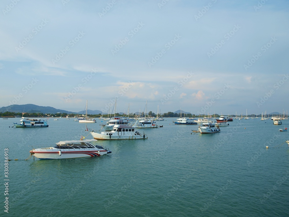 Boats and speedboats anchored in a sea bay against the backdrop of the land, green hill, forest and mountain in sunny day