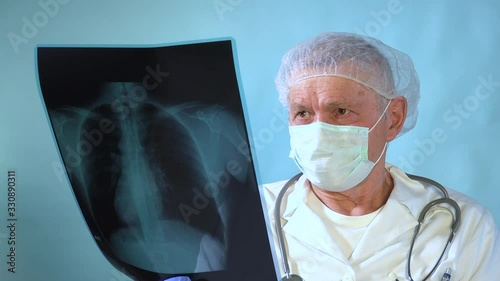 Serious aged male surgeon holding radiography of patient, senior doctor checking chest x-ray film at ward hospital, old caucasian lung specialist looking pulmonary disease, medium shot