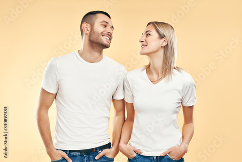 Young happy couple in love look to each other over beige background
