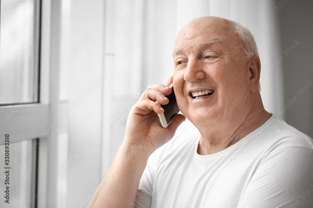 Portrait of elderly man talking by phone near window Portrait of elderly man talking by phone near window