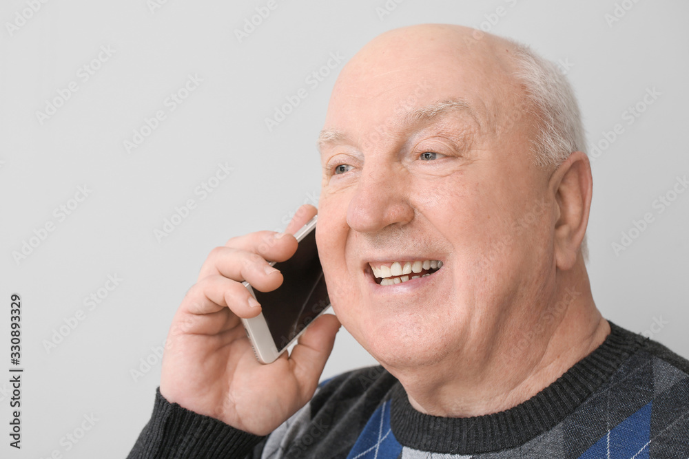 Portrait of elderly man talking by phone on light background Portrait of elderly man talking by phone on light background