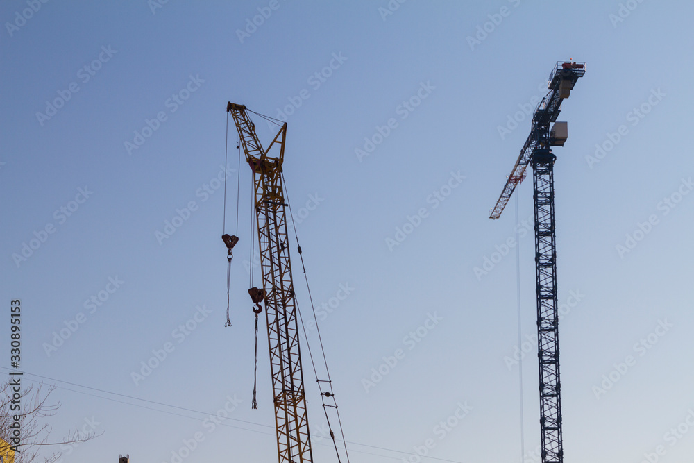Two construction cranes on the blue sky background. Backlit images. Two construction cranes on the blue sky background. Backlit images.
