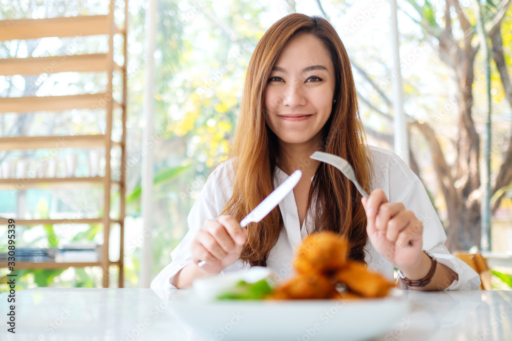 Closeup image of a beautiful asian woman using knife and fork to eat fried chicken in restaurant Closeup image of a beautiful asian woman using knife and fork to eat fried chicken in restaurant