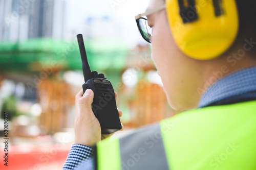 Young asian engineers are working on the construction site. Wear a yellow earmuff sound protection and uniform staff. Hand holding portable radio transceiver for communication