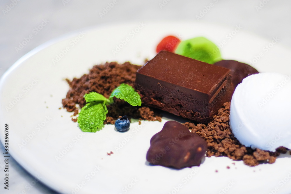 Close up sweet dessert brown pieces of chocolate and vanilla ice-cream with mint leaves on white plate. Close up sweet dessert brown pieces of chocolate and vanilla ice-cream with mint leaves on white plate.