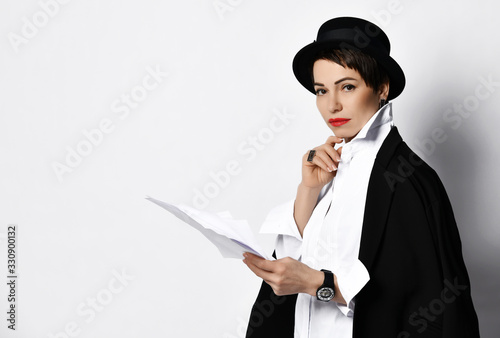 Woman in stylish old fashion boater hat and black jacket holding sheets of paper looks at us gravely