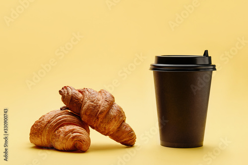 A pair of croissants and a disposable cup of coffee or tea