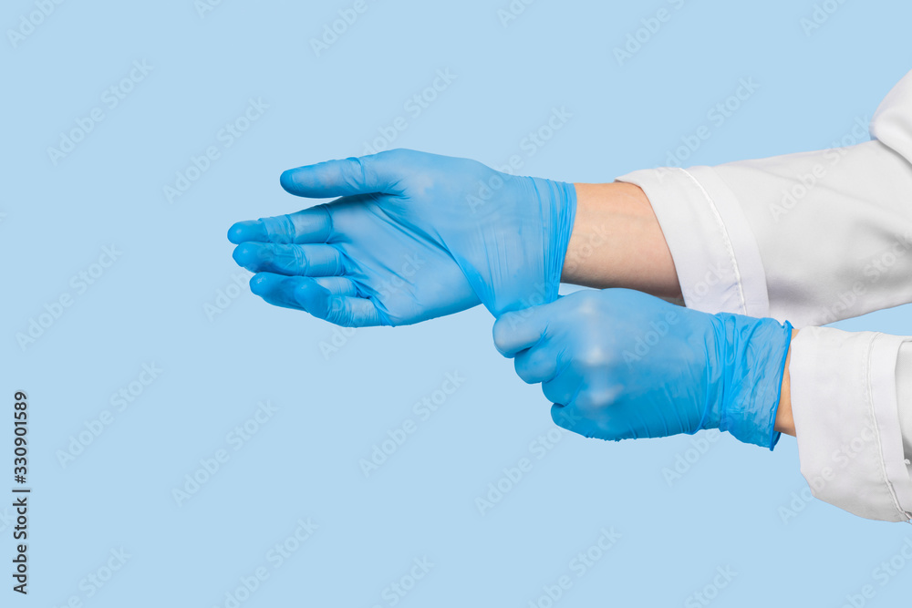 The doctor puts on sterile gloves on a blue background. Infection control concept. Danger of spread of infection The doctor puts on sterile gloves on a blue background. Infection control concept. Danger of spread of infection