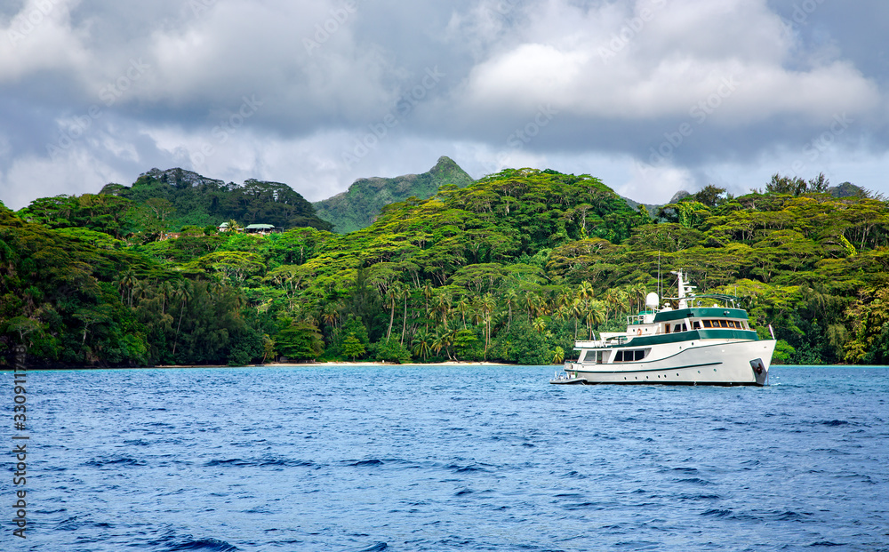 Pleasure ship anchored in a calm blue lagoon near the Tahaa island in the Pacific ocean, French Polynesia.