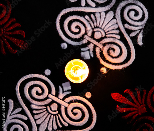 rotated view of tea lamp and white red rangoli on black background. deepawli concept photo