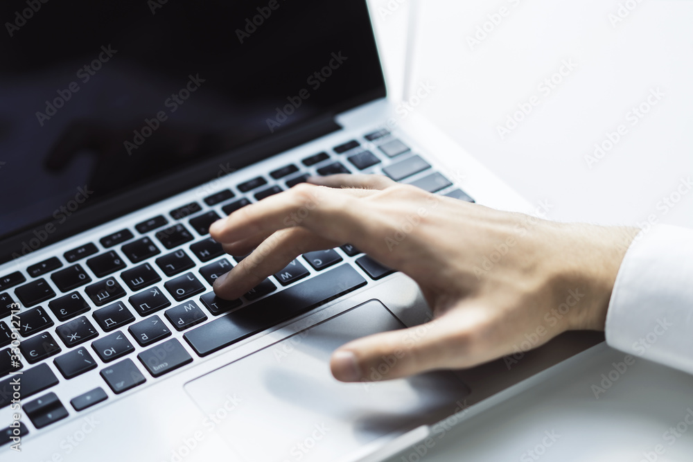 Man typing on laptop keyboard in sunny office, business and technology concept. Close up