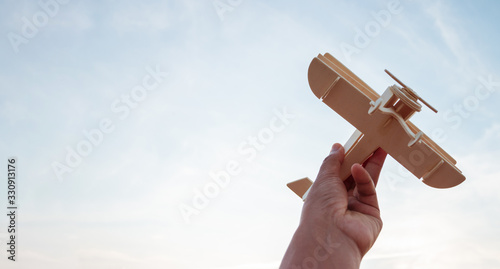 Freedom concept, human hand holding wooden plane on the sunset sky background