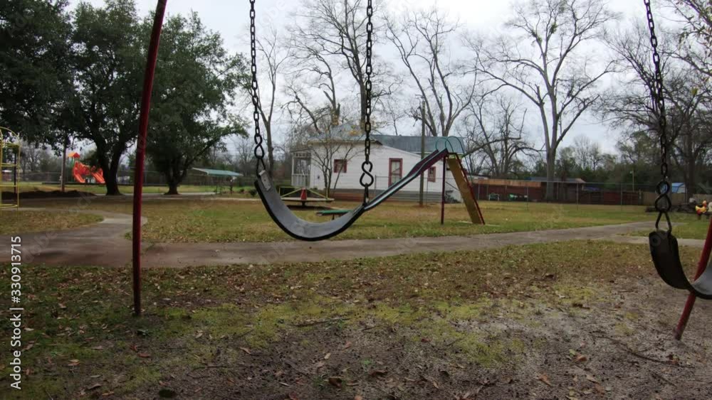 Swings and other equipment on a vacant playground in a park with one swinging on its own Swings and other equipment on a vacant playground in a park with one swinging on its own