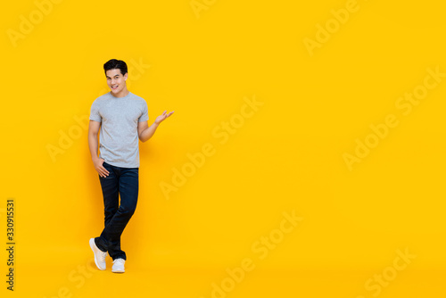 Handsome young Asian man smiling and standing with open hand gesture photo