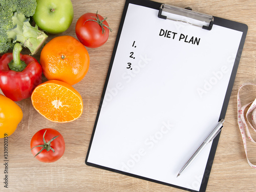 Clipboard with diet plan paper, fresh colorful vegetables, fruits and measuring tape on wooden background with copy space. Healthy diet, nutrition and weight loss concept.