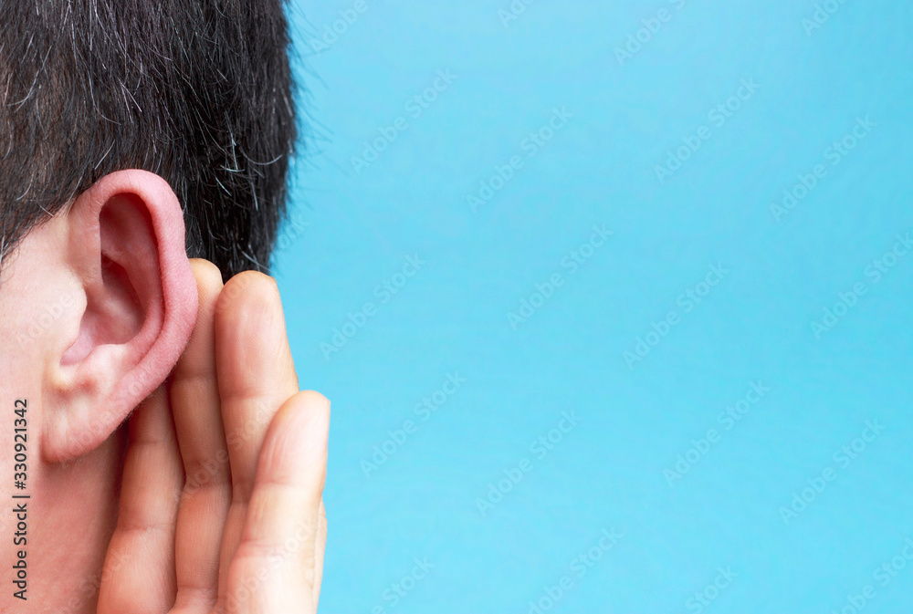Obraz premium The man listens attentively with her palm to her ear close-up, blue background