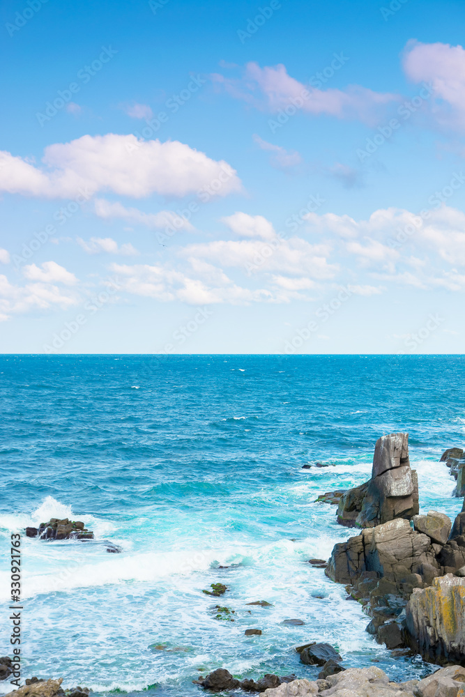 rocky sea shore in the afternoon. blue waves crashing the coast. fluffy clouds above the horizon. rocky sea shore in the afternoon. blue waves crashing the coast. fluffy clouds above the horizon.